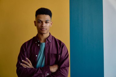 Modern ofisin renkli duvarlarına yaslanmış kendinden emin genç iş adamının portresi.