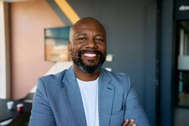 Spor ceketli Afrikalı olgun iş adamının portresi modern ofiste kameraya gülümsüyor.