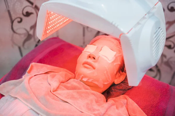 Beauty spa technology concept, a machine that projects red LED light onto the face of a leaning Asian woman.