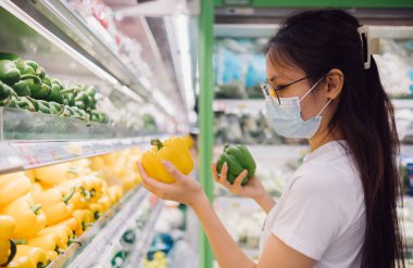 Yüz maskeli Asyalı kadın dolmalık biber, organik yaşam tarzı ve vegan konsepti için alışveriş yapıyor..