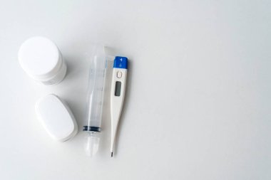 Dijital termometre, parmak ucu oksimetresi, ilaç şişesi, burun şırıngası tüpü, beyaz arka plan, düz döşeme tarzı, ev tıbbi gereç konsepti.