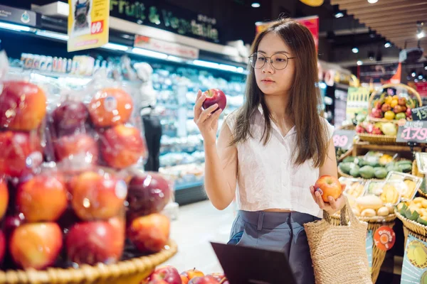 an asian woman holding for shopping an apple in a grocery store, vegan lifestyle concept.