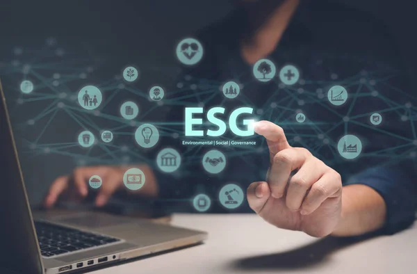 Man touching ESG hologram, a concept of sustainable development that combines environment, society, and governance. The hologram consists of icons of trees, robots, bank, heart, family, factory, air, money, data, and network.