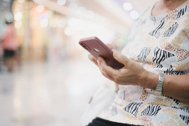 Yaşlı Taylandlı bir kadın dijital dünyada hızlı bir alışveriş merkezinde akıllı telefonunu kullanarak rahatça dolaşır. Bu resim modern teknolojinin, sosyal medyanın ve etkin bir yaşam tarzının kesişiminin özetini içerir, d 'nin içeriğini vurgular.