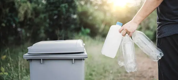 A person recycles plastic bottles in a trash can. This is an example of how to reduce carbon emissions and help the environment.