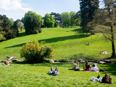 Paris, Fransa - 15 Nisan 2022: The Parc des Buttes Chaumont, manzaranın doğasını tasvir eden manzara, bazı insanların tatil kazanç sağladığı yeşil çimenler