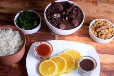 traditional Brazilian food feijoada with beans, pork, bacon, sausage with cabbage, rice, salad, spices and pepper. rustic kitchen.
