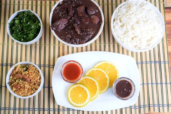 traditional Brazilian food feijoada with beans, pork, bacon, sausage with cabbage, rice, salad, spices and pepper. rustic kitchen.