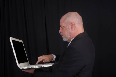 Siyah arka plana karşı beyaz gömlekli, orta yaşlı yakışıklı bir adam. Bilgisayar kullanan kendine güvenen bir iş adamı