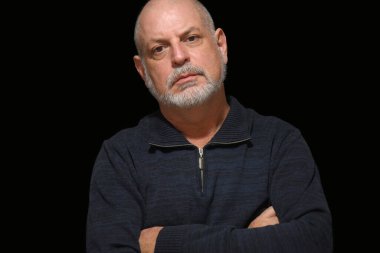 Beyaz sakallı yetişkin bir adam siyah arka planda tek başına ileriye bakıyor.