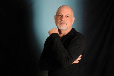 Siyah gömlekli beyaz sakallı beyefendi stüdyoya giriyor.