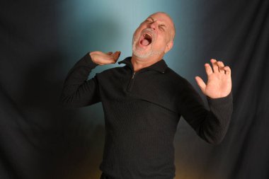 Siyah gömlekli beyaz sakallı beyefendi stüdyoya giriyor.