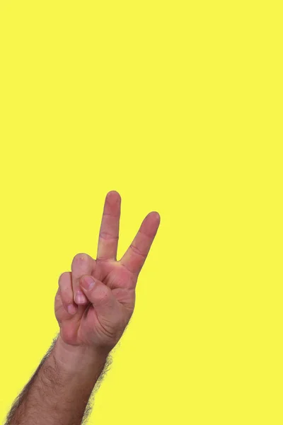 hand making peace and love gesture fingers raised in v isolated on yellow background