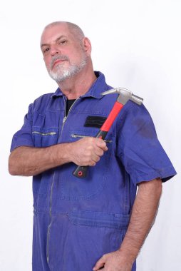 Mavi iş elbiseli beyaz sakallı adam beyaz arka planda çekiç aleti tutuyor.