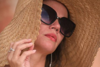 Plaj modelinde genç ve rahat bir kadın. Yaz mevsimi, açık renk kıyafetler, ruj, güneş gözlüğü, saç ve doğa kilidi.