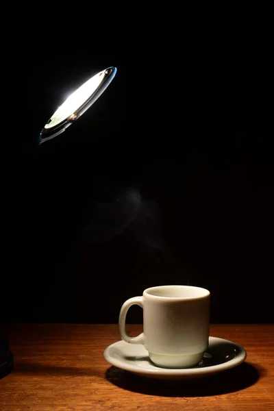 cup of coffee on wooden table with light coming from above image