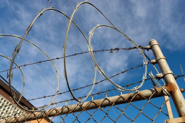 Dikenli tel tel, tel örgülerde mavi gökyüzü ve bulutlar arka planda..