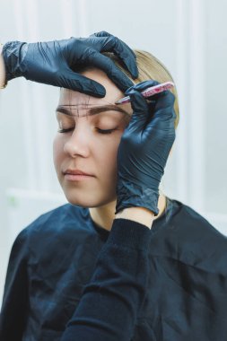 Kalıcı makyajdan önce profesyonel kaş haritalama işlemi sırasında genç bir kadın.