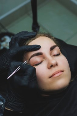 Çekici bir kadın yüzüne kaş makyajı yapan bir güzellik uzmanı.