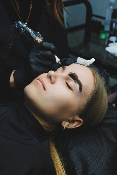 Permanent makeup. Beauty procedures. The master applies a tattoo on the eyebrows. Professional facial microblading. Women\'s cosmetology device.