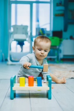 8 aylık küçük bir çocuk yerde oturuyor ve tahta oyuncaklarla oynuyor. Çocukların ekolojik oyuncakları