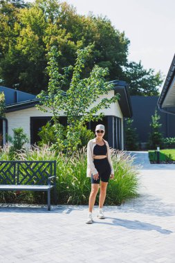 Siyah bluzlu ve şortlu, çok büyük bir ceket giyen zayıf, genç, şık bir kadın. Şık bir kız sokakta yürüyor. Şık bir yaz moda kıyafeti. güneş gözlüğü,