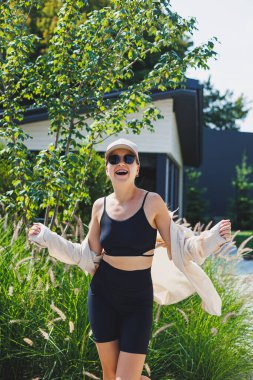 Siyah bluzlu ve şortlu, çok büyük bir ceket giyen zayıf, genç, şık bir kadın. Şık bir kız sokakta yürüyor. Şık bir yaz moda kıyafeti. güneş gözlüğü,