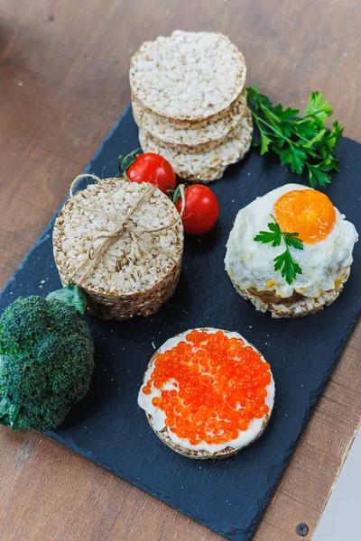Diet rice breads, cherry tomatoes and fresh caviar and parsley on a dark background. Snack bread. View from above. Dietary fiber. Healthy Eating