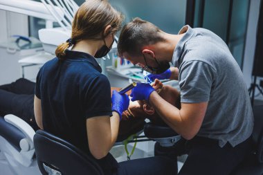 Diş tedavisiyle. Dişçiyle randevusu olan genç bir adam. Doktor ve asistan, dişçi muayenehanesinde hastanın dişlerini tedavi eder.