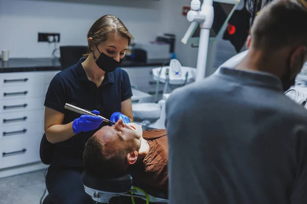 stock image Dental treatment of teeth. A young man at a dentist's appointment. A doctor and an assistant treat a patient's teeth in a dental office