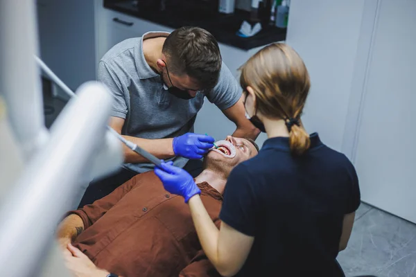 Dental treatment of teeth. A young man at a dentist's appointment. A doctor and an assistant treat a patient's teeth in a dental office