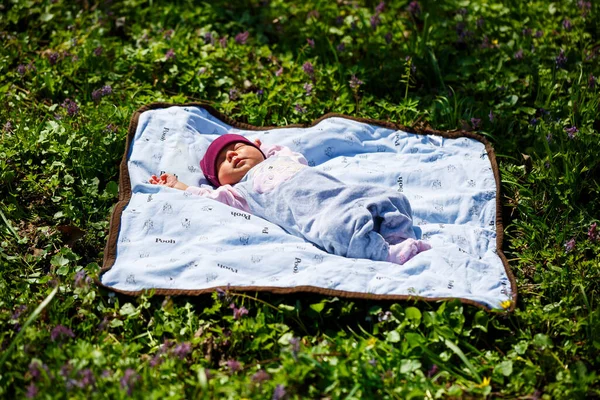 赤いキャップの赤ちゃんの写真の肖像画は 緑の芝生の上で遊ぶ白い上にあります 春は通りにあり 太陽は子供に輝いています — ストック写真
