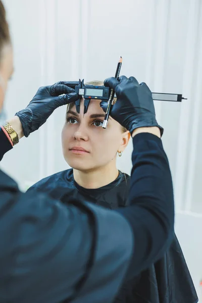 permanent eyebrows tattoo. permanent tattoo master checks the distance on the eyebrow sketch before the beauty procedure. beauty concept, free space