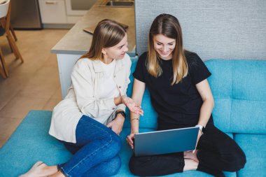 Evdeki kanepede oturup dizüstü bilgisayar kullanarak film izleyen iki güzel genç kadın, oturma odasındaki kanepede oturan iki bayan arkadaş..