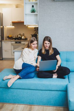 Evdeki kanepede oturup dizüstü bilgisayar kullanarak film izleyen iki güzel genç kadın, oturma odasındaki kanepede oturan iki bayan arkadaş..