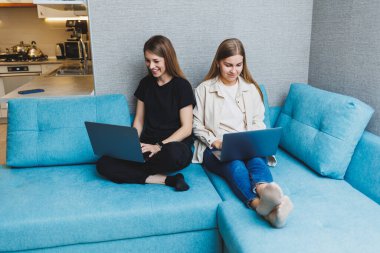 Oturma odasında kanepede dizüstü bilgisayar kullanarak çalışan iki tatlı kadın. Arkadaşlar, arkadaşlık, birlikte zaman geçirmek. Kız arkadaşlar kanepede oturup film izliyorlar.