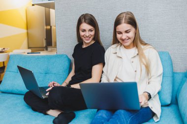 Oturma odasında kanepede dizüstü bilgisayar kullanarak çalışan iki tatlı kadın. Arkadaşlar, arkadaşlık, birlikte zaman geçirmek. Kız arkadaşlar kanepede oturup film izliyorlar.