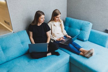 Oturma odasında kanepede dizüstü bilgisayar kullanarak çalışan iki tatlı kadın. Arkadaşlar, arkadaşlık, birlikte zaman geçirmek. Kız arkadaşlar kanepede oturup film izliyorlar.