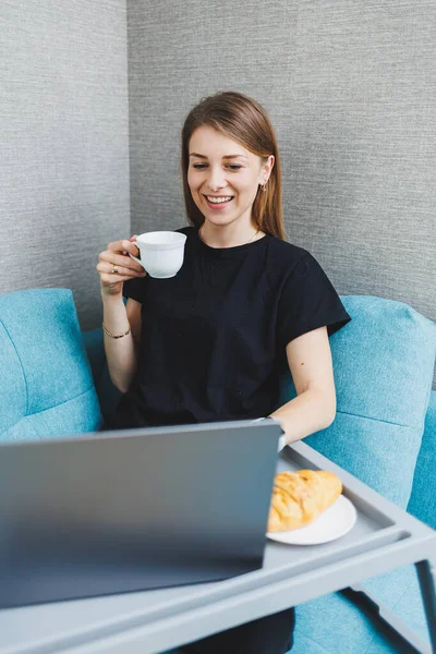 年轻女性喜欢在家里坐在沙发上 一边用笔记本电脑喝早茶 一边在电脑上打字 一边在网上玩乐 一边在沙发上放松地和朋友聊天 — 图库照片