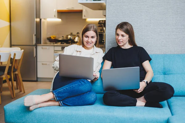 stock image Two cute women are chatting with their friends via video call using a laptop in the living room. Friends, friendship, time together. Girlfriends are sitting on the couch and watching a movie