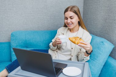 Genç, mutlu, serbest çalışan bir kadın, kanepede oturuyor, dizüstü bilgisayarda film izliyor, çalışıyor, blog yazıyor, rahatlıyor ve internette sohbet ediyor. Yüksek kalite fotoğraf