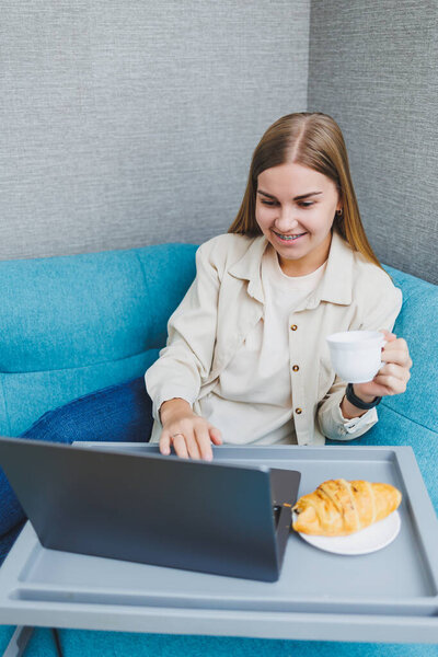 Молодая счастливая женщина-фрилансер сидит на диване, работает над проектом, смотрит кино на ноутбуке, учится, ведет блоги, отдыхает и отдыхает в Интернете. Высокое качество фото