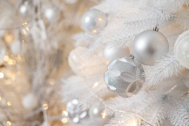 Beyaz bir Noel ağacı gümüş plastik oyuncaklarla süslenir. Yeni yıl için parlak şenlik dekorasyonu