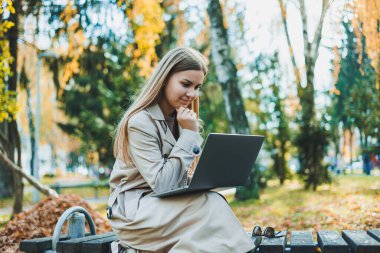 Sonbahar parkında dizüstü bilgisayarıyla oturmuş internette çalışan tatlı bir kız öğrenci. Parkta çalışan mutlu kadın..