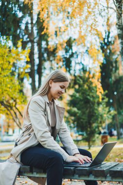 Sonbahar parkında dizüstü bilgisayarıyla oturmuş internette çalışan tatlı bir kız öğrenci. Parkta çalışan mutlu kadın..