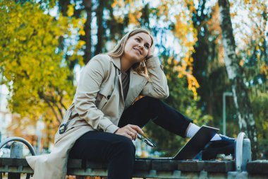 Sonbahar parkında dizüstü bilgisayarıyla oturmuş internette çalışan tatlı bir kız öğrenci. Parkta çalışan mutlu kadın..