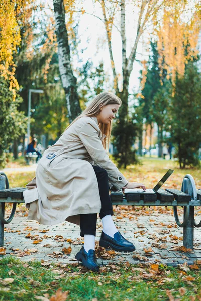 秋の公園にラップトップで座ってオンラインで働いているかわいい女性学生 公園の外で働く幸せな女性 — ストック写真