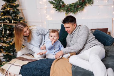 Küçük bir oğlu olan neşeli genç bir çift Noel ağacının yanındaki yatakta oynuyorlar. Yeni yıl içleri yatak odasında. Oyuncaklı Noel ağacı. Şenlikli aile ortamı.