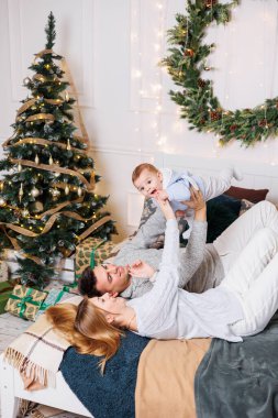 Küçük bir oğlu olan neşeli genç bir çift Noel ağacının yanındaki yatakta oynuyorlar. Yeni yıl içleri yatak odasında. Oyuncaklı Noel ağacı. Şenlikli aile ortamı.