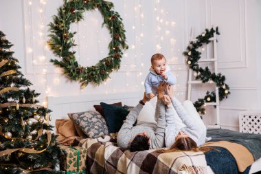 Küçük bir oğlu olan neşeli genç bir çift Noel ağacının yanındaki yatakta oynuyorlar. Yeni yıl içleri yatak odasında. Oyuncaklı Noel ağacı. Şenlikli aile ortamı.